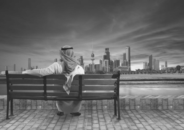 Homme assis sur un banc regardant la ville du Koweït